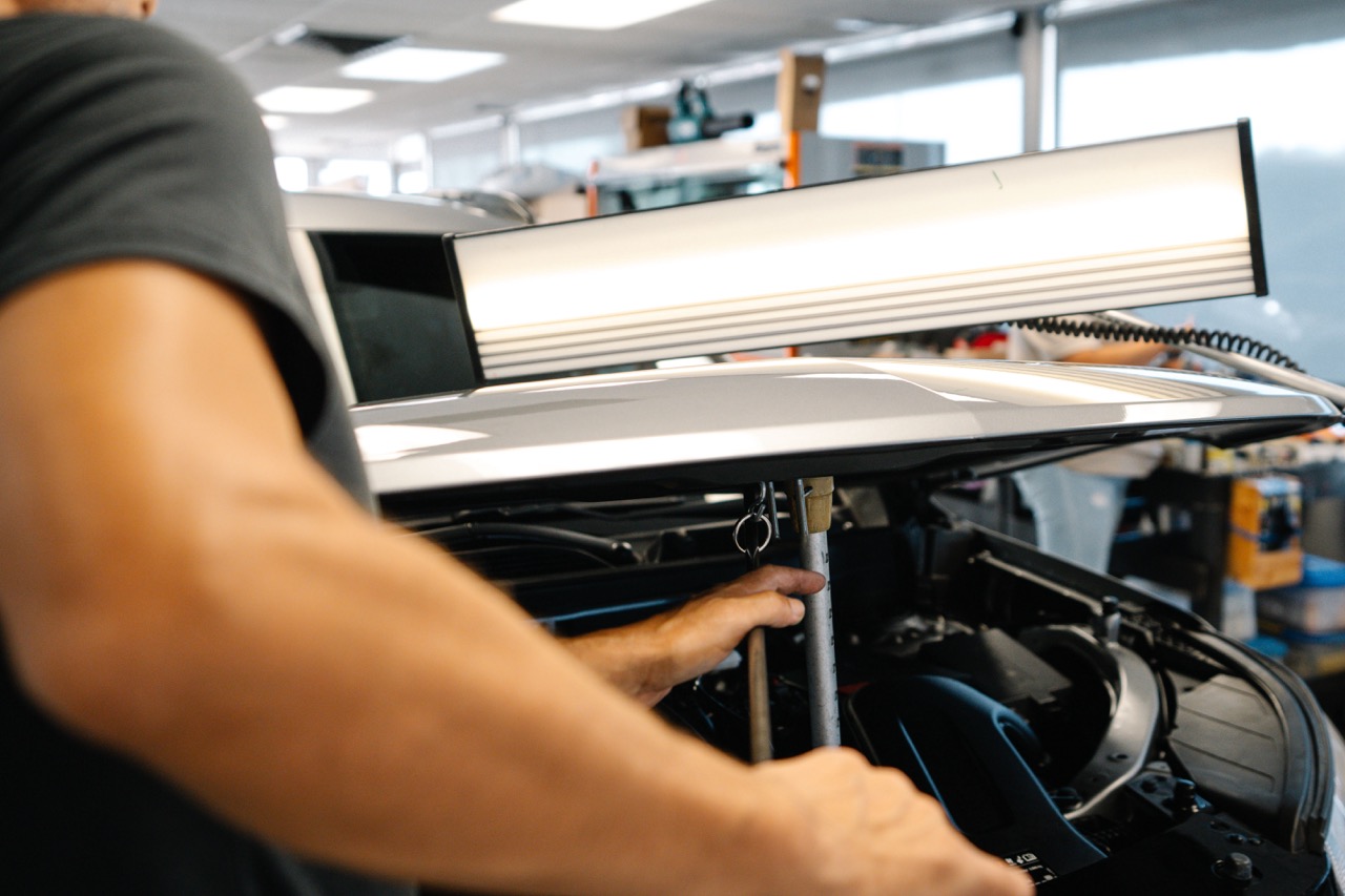 Person identifying dents on a panel using a specialized paintless dent repair light