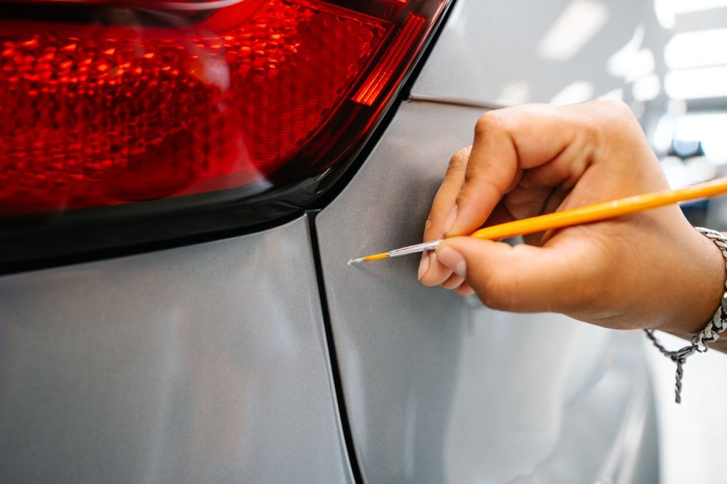 Person's hand touching up paint on rear bumper of car